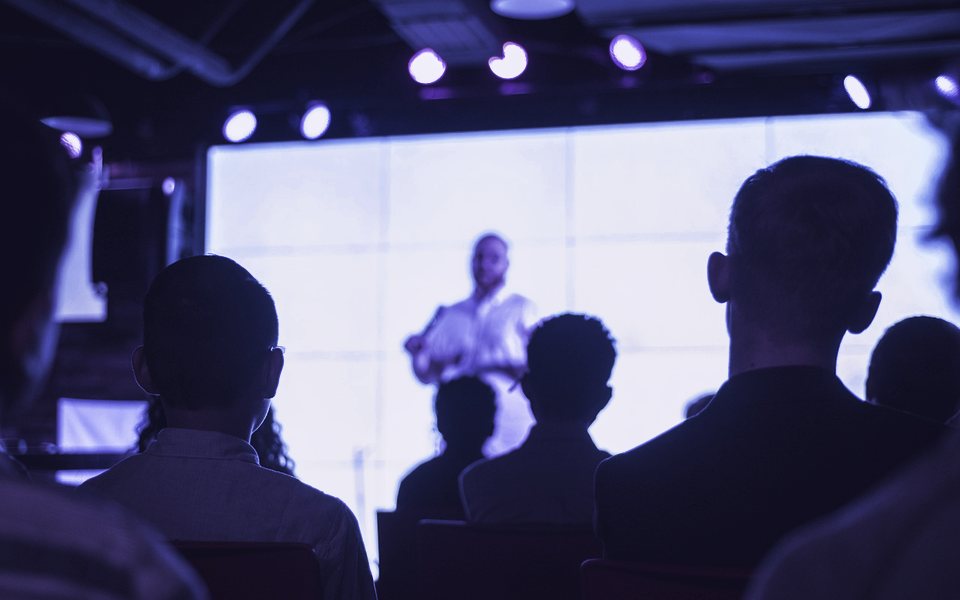 An audience watching a speaker on a large screen